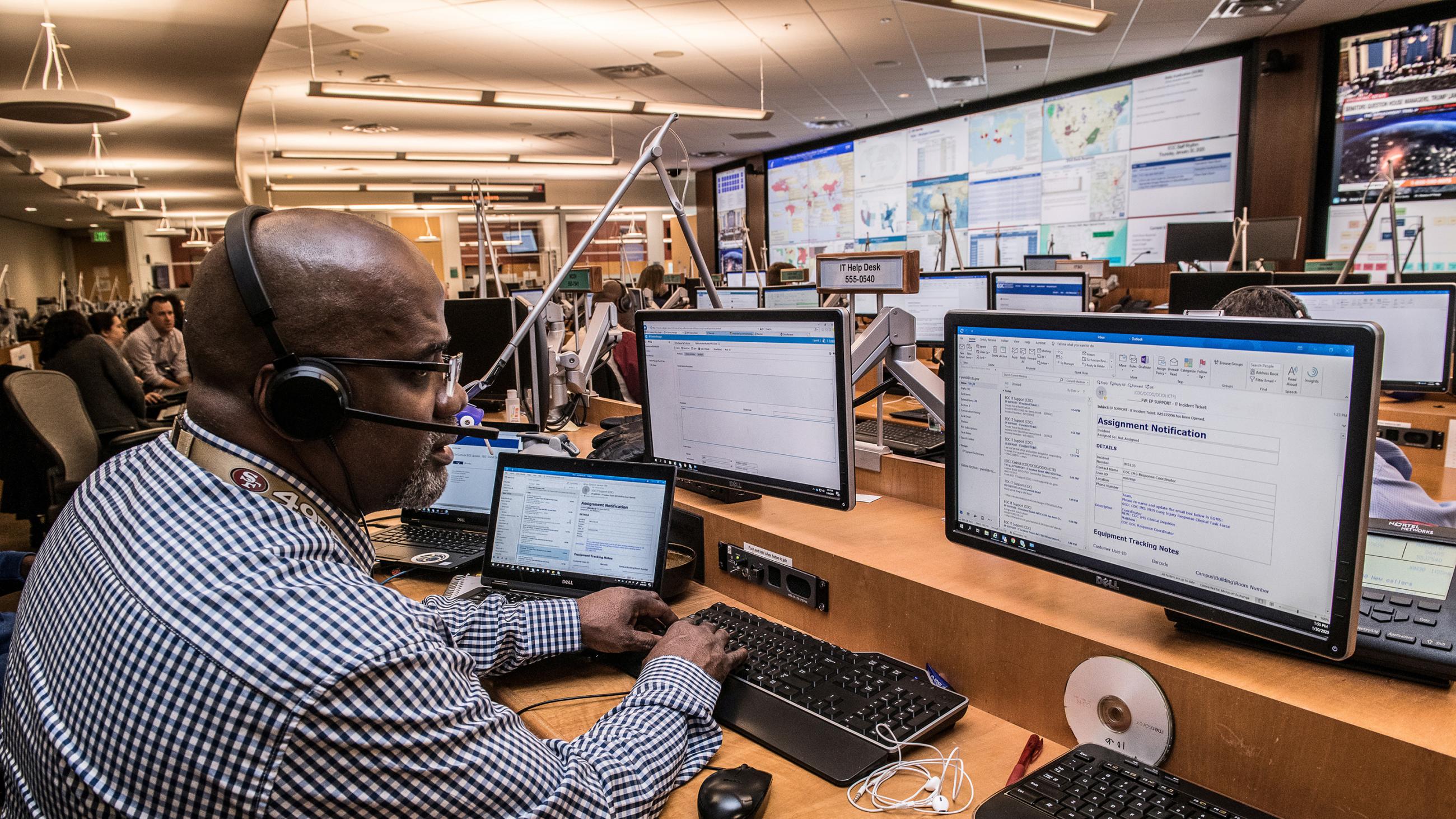 Picture shows a man in a large operations room with numerous huge display screens showing data. 