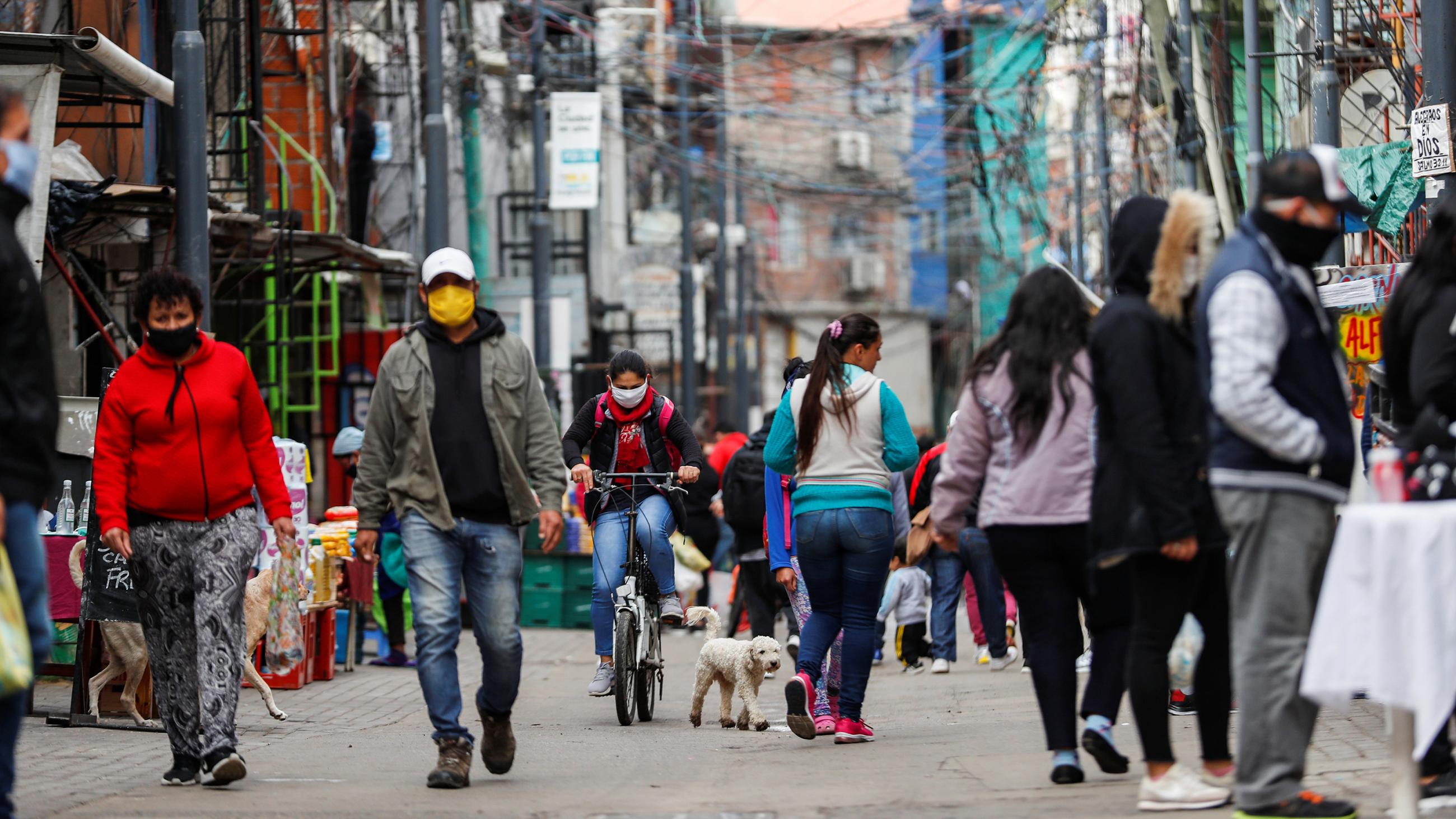 Picture shows a neighborhood street scene with lots of people wandering the streets wearing facemasks.  