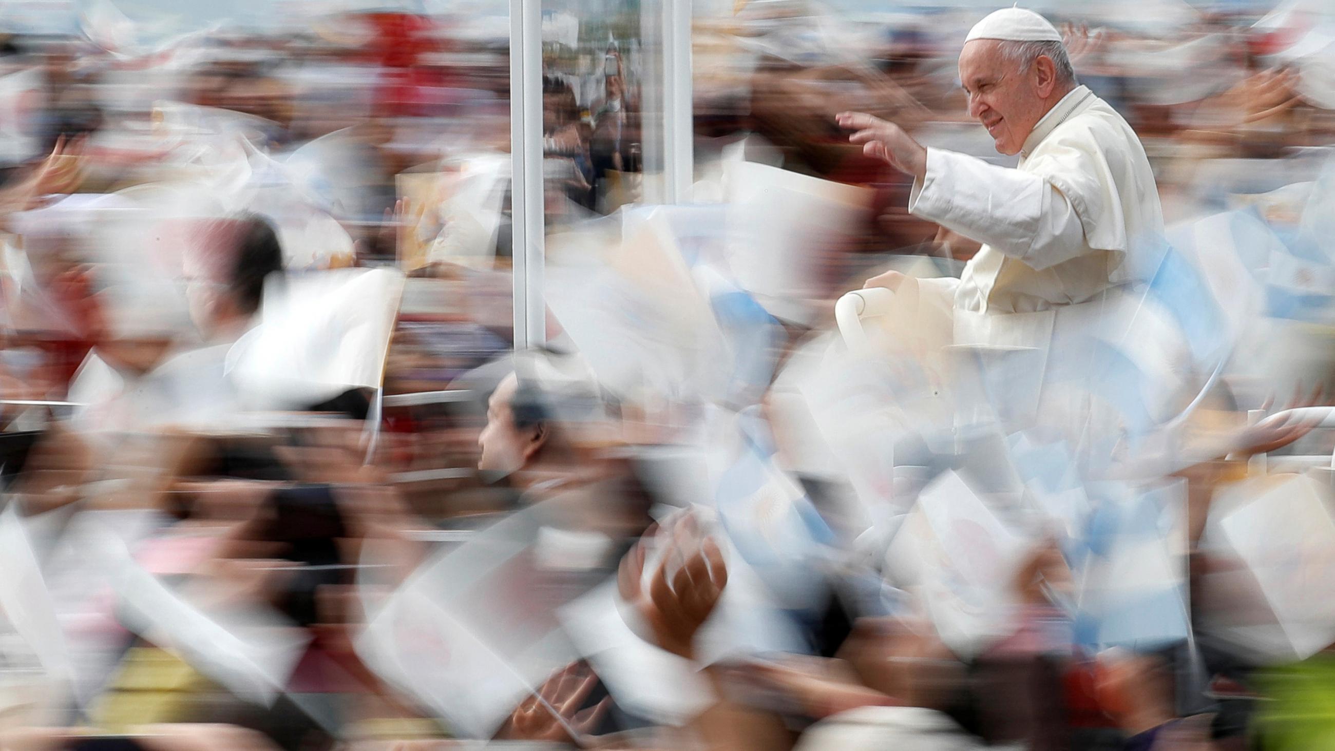 The photo shows the pope in clear focus while all the bustling crowds around him are moving and out of focus. 