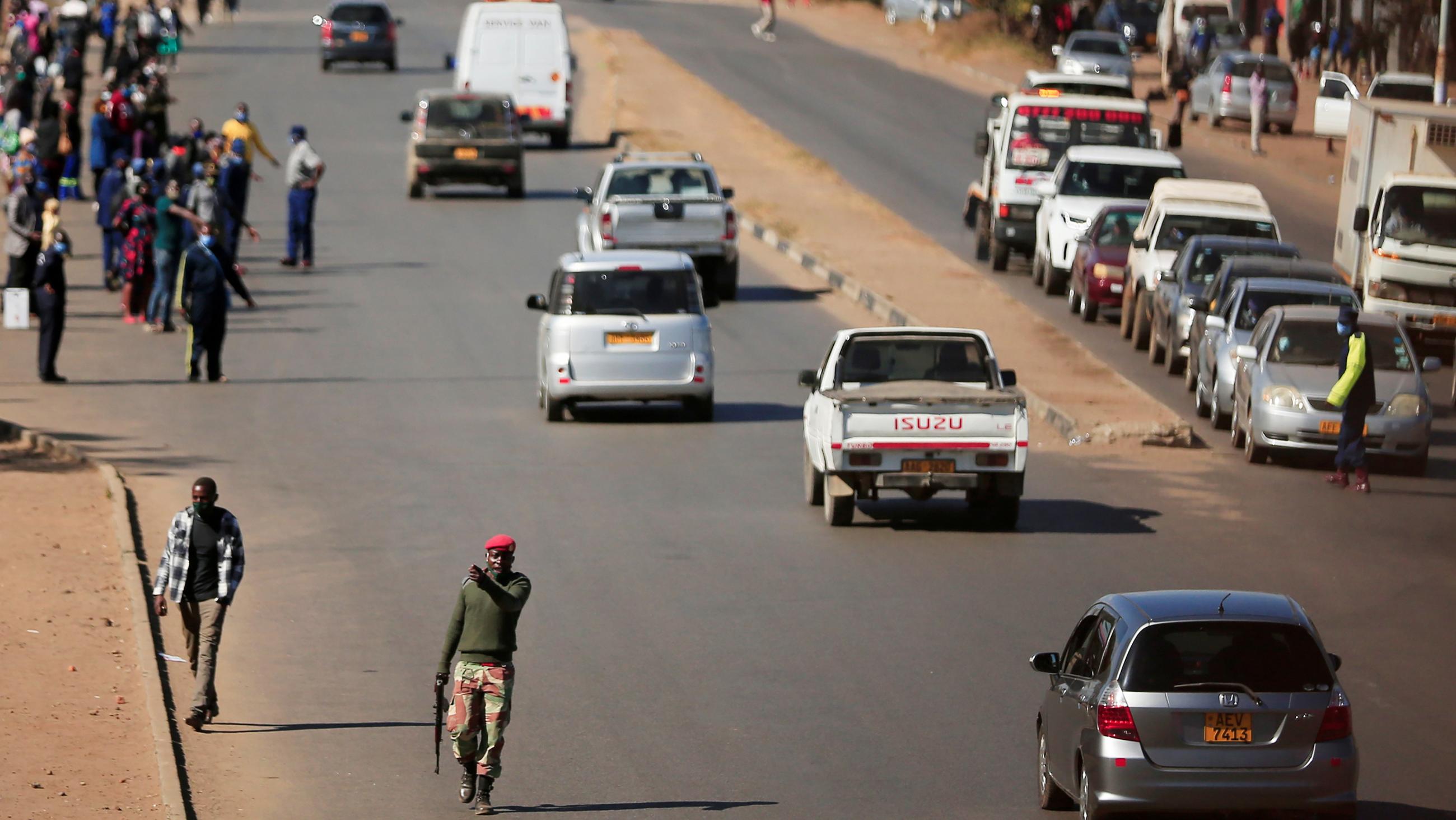 The photo shows a street with cars, soldiers and protesters. 