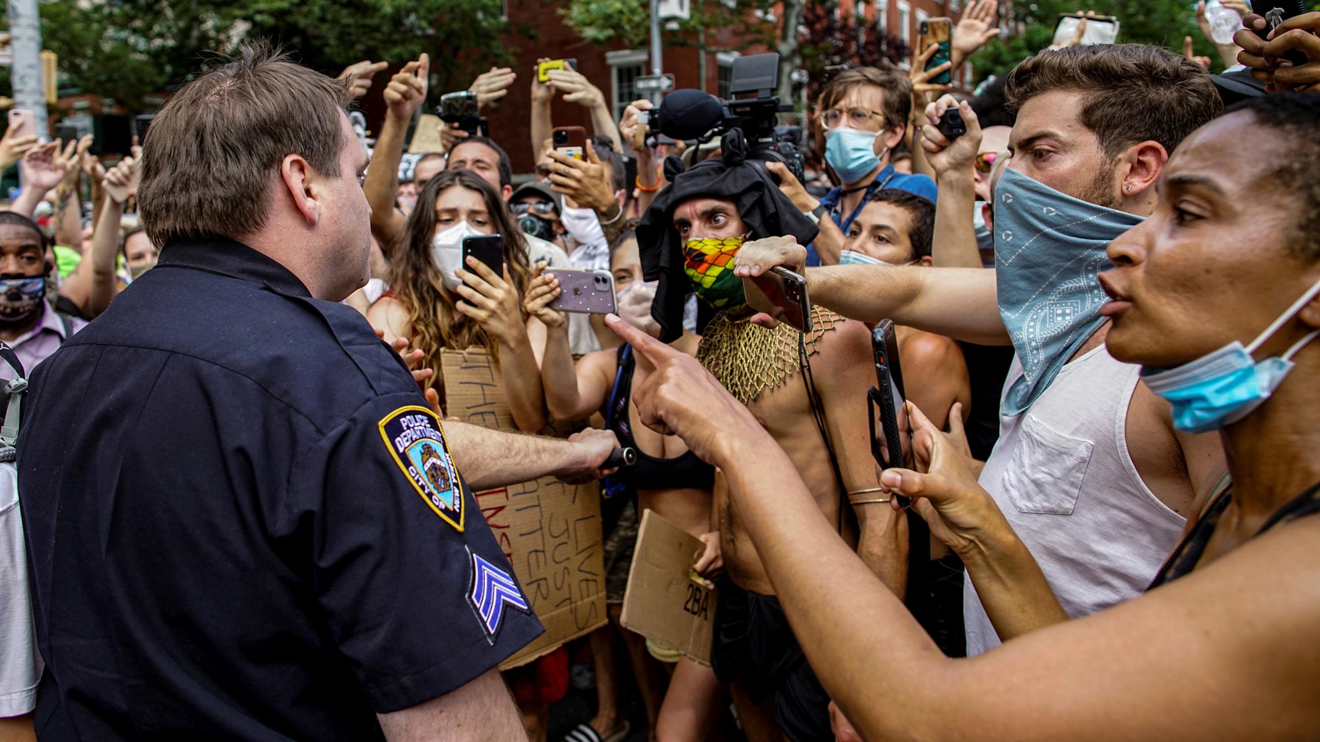 The photo shows a single officer surrounded by people protesting. 