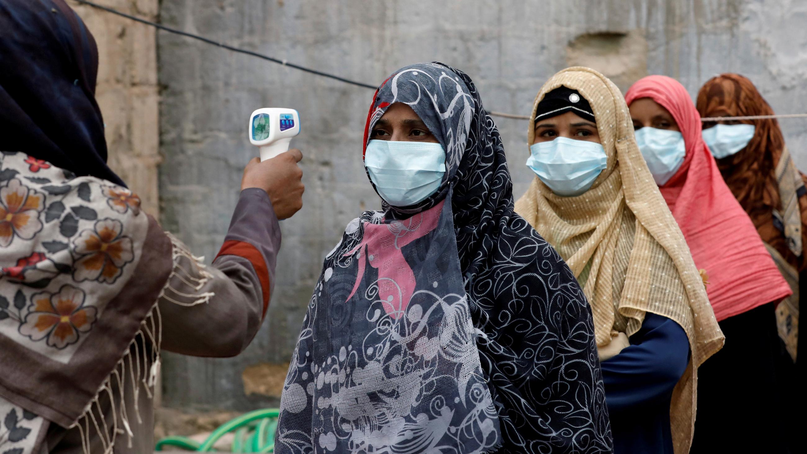 The photo shows several people lined up while their temperature is being checked. 