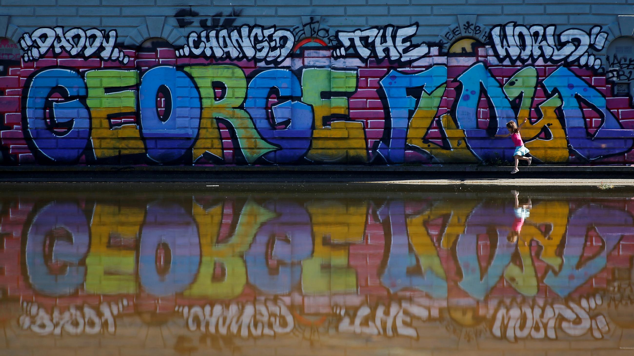 The photo shows a child walking in front of a large colorful mural of George Floyd's name. 