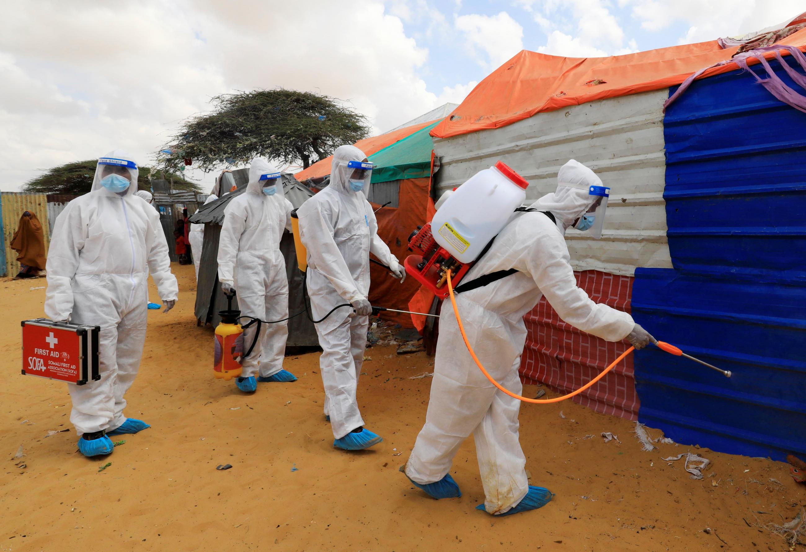 Men wearing body-covering white suits and are members of Somali First Aid Association spray disinfectants in an effort to stop the spread of COVID-19 at a camp for internally displaced people in Mogadishu, Somalia on April 18, 2021