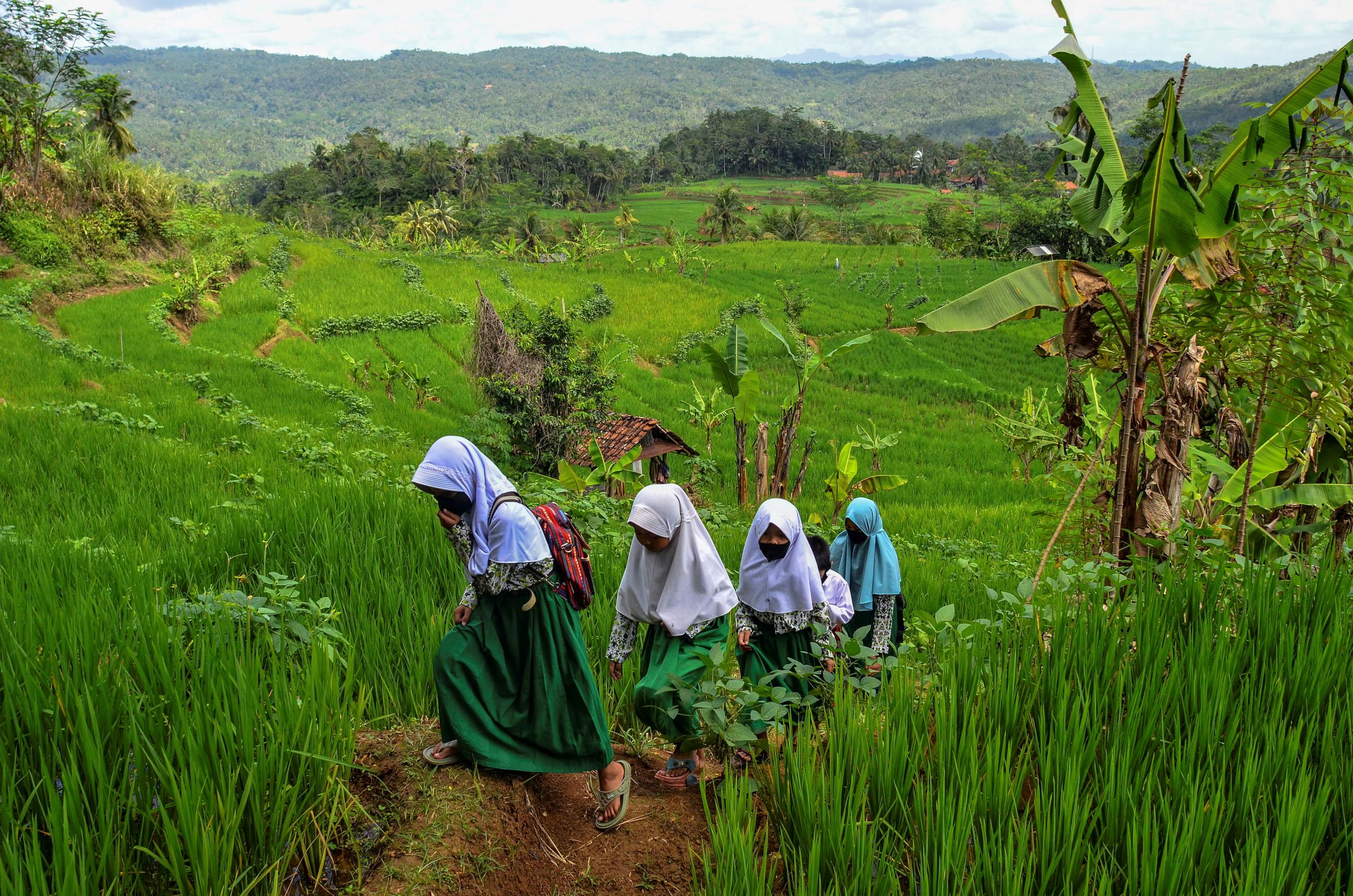 Students wearing face masks walk home across a green expanse of grass after class as schools reopen on a trial basis during the COVID-19 pandemic, in Ciamis, West Java, Indonesia, on September 9, 2021.