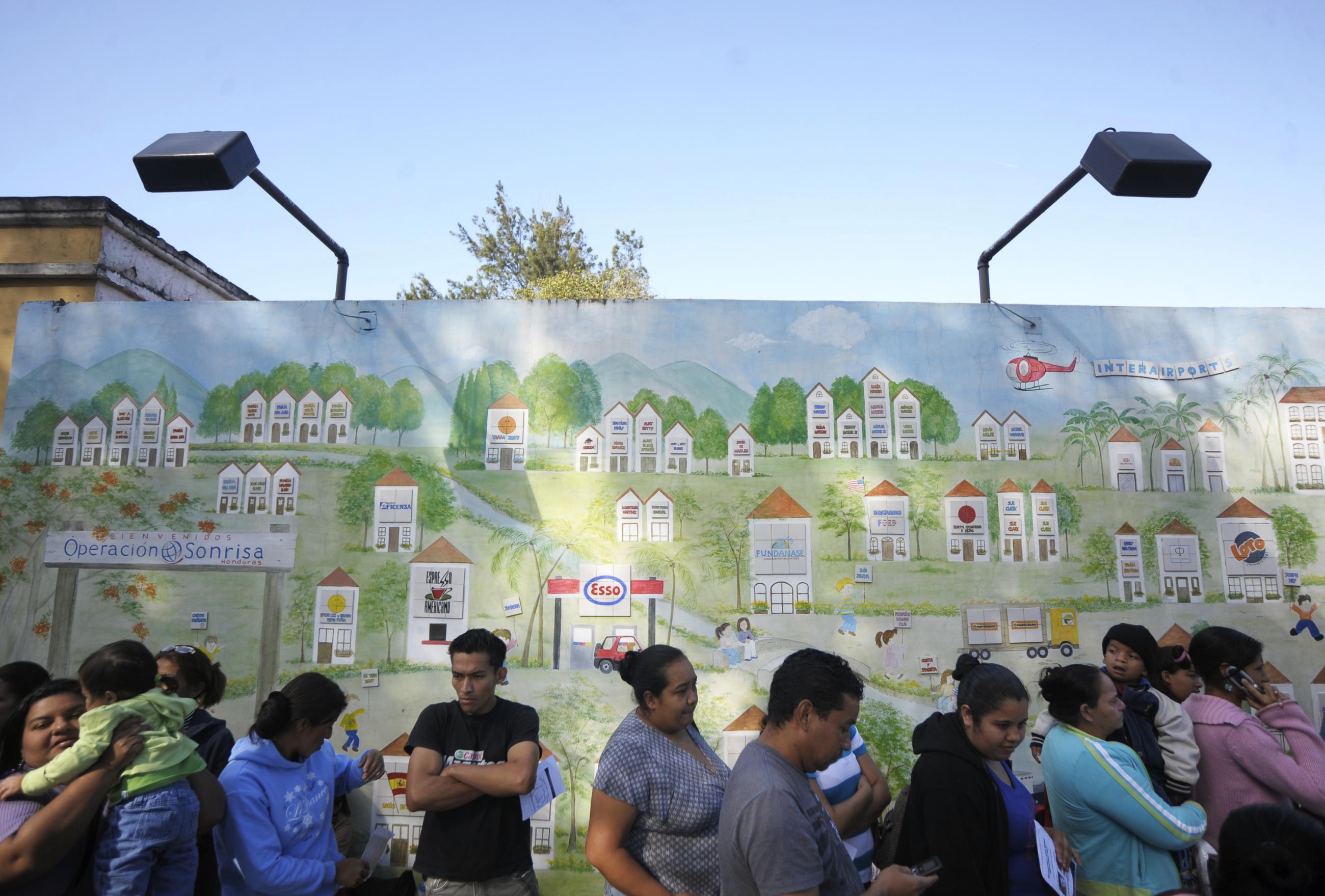 Parents stand in front of a big wall decorated with a mural and wait for doctors with Operation Smile, an organization that provides free surgery for children who have cleft palates and other facial deformities, to give medical evaluations for their children at Hospital San Felipe, in Tegucigalpa, Honduras.