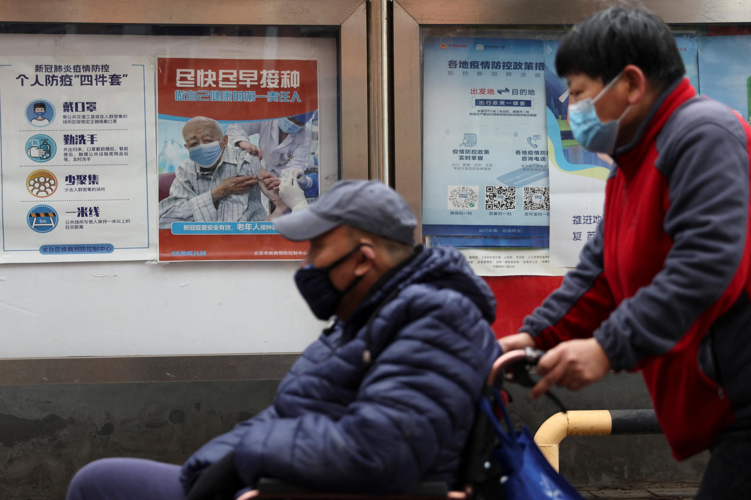 People pass by a poster encouraging elderly people to get vaccinated against COVID-19, near a residential compound in Beijing, China, March 30, 2022.