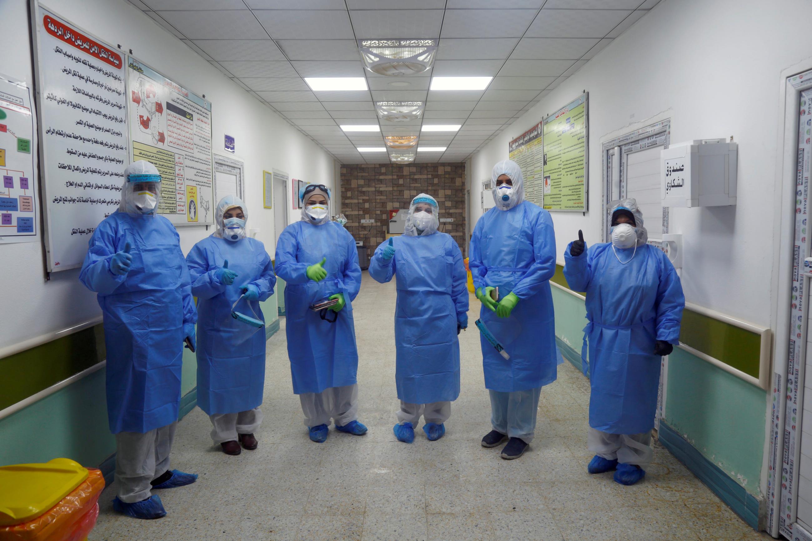 Nurses and volunteers wearing protective suits and face masks pose for a photo at a hospital.