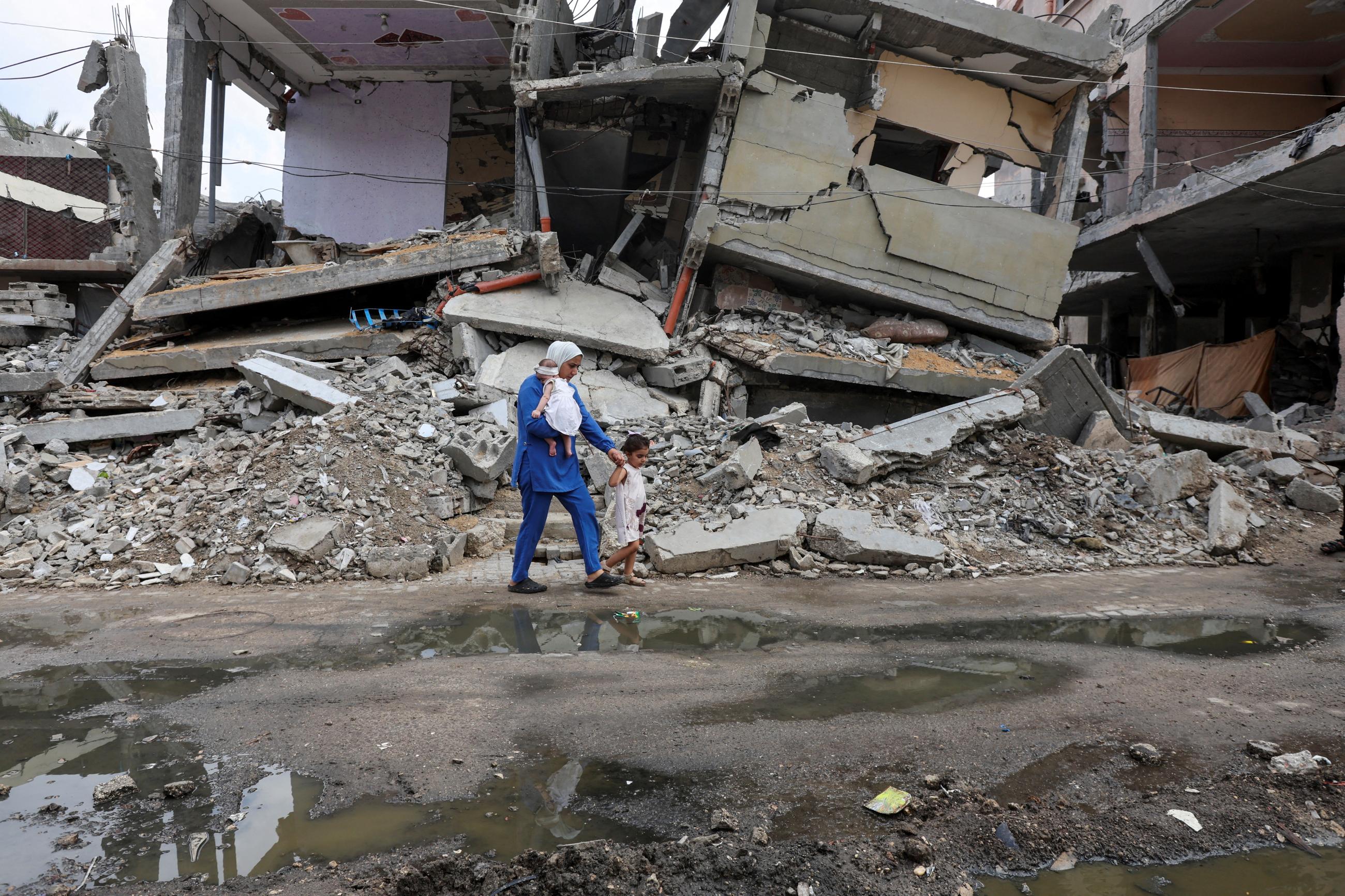 A displaced Palestinian mother walks past the rubble of a house with her child after they got vaccinated against polio.