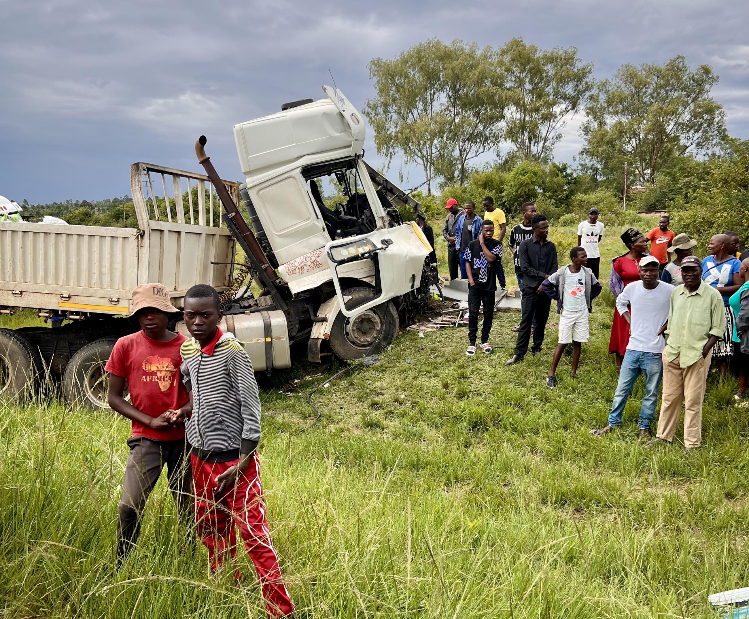 People stand beside a tractor trailer that was involved in a head-on collision with a bus, in Macheke, Zimbabwe, in January 2024.