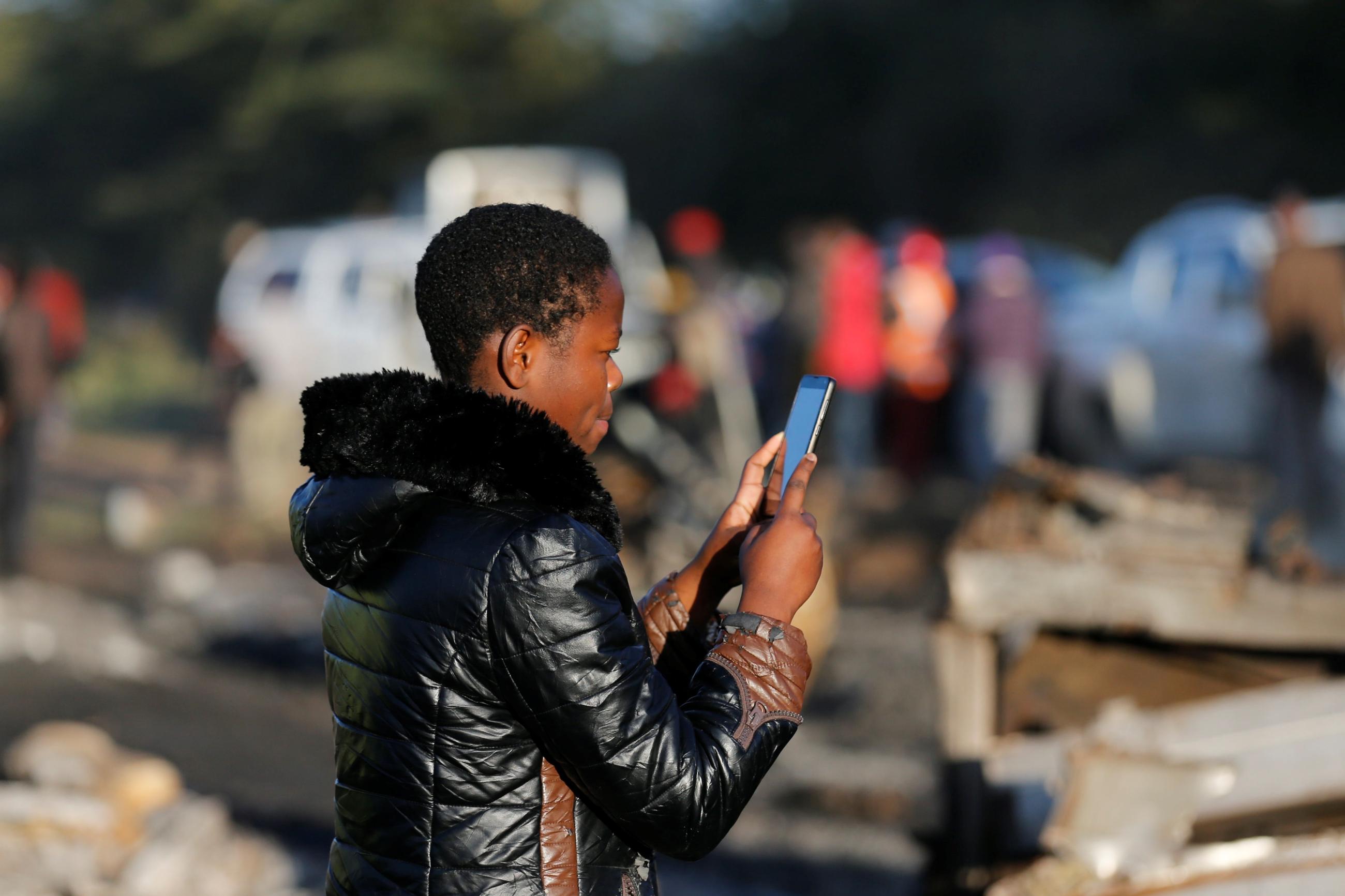 A woman uses her phone to take pictures of the wreckages of cars burnt after an accident involving a tanker.
