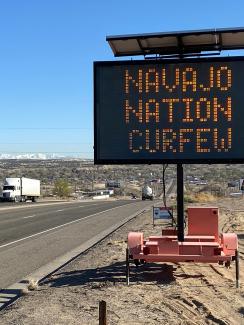 Picture shows a portable electronic road warning sign programmed to display the message "NAVAJO NATION CURFEW." 