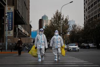 Pandemic prevention workers in protective suits cross a street as COVID-19 outbreaks continue.