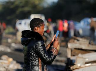 A woman uses her phone to take pictures of the wreckages of cars burnt after an accident involving a tanker.