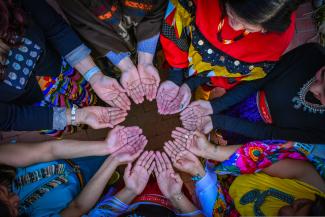 Changing Woman Initiative board and staff members, wearing traditional clothing from their respective tribes, connect with open hands to symbolize their acceptance of prayers and blessings.