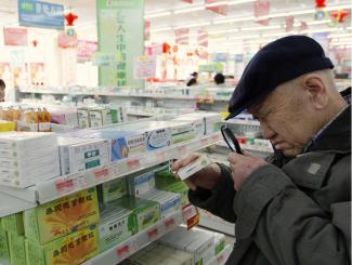 An elderly man uses a magnifier to see the descriptions on a pack of medicine at a pharmacy.